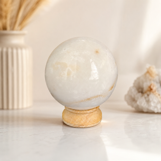 Witte maansteen bol van 6 cm en 334 gram op houten standaard als luxe edelsteen woondecoratie.